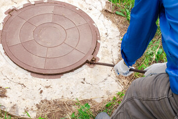 A plumber opens a manhole cover on a concrete well with a crowbar. Inspection and maintenance of water and sewer wells