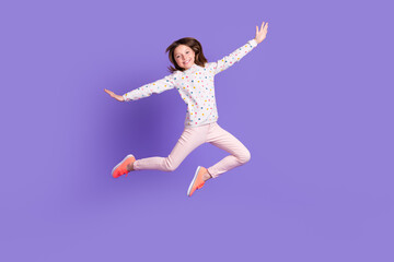 Fototapeta na wymiar Full length photo of carefree pretty little girl dressed dotted pullover arms sides jumping high isolated purple color background