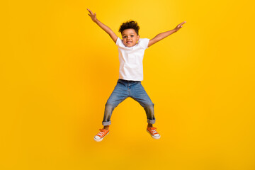 Full length photo of sweet excited little boy dressed white t-shirt jumping high arms sides isolated yellow color background