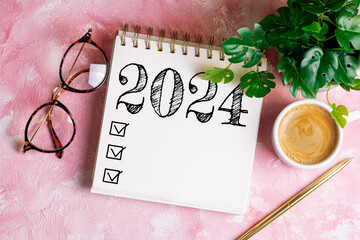 New year resolutions 2024 on desk. 2024 goals list with notebook, coffee cup, plant on pink table. Resolutions, plan, goals, action, checklist, idea concept. New Year 2024 resolutions, copy space