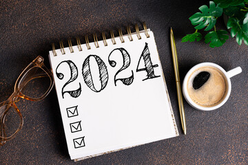 New year resolutions 2024 on desk. 2024 goals list with notebook, coffee cup, plant on table....