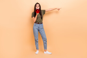 Fototapeta na wymiar Full length photo of impressed excited lady wear khaki t-shirt shouting bullhorn pointing empty space isolated beige color background