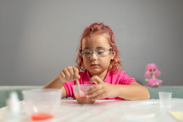 A beautiful little girl with crimson hair, wearing a pink shirt and safety glasses is playing educational games at the table