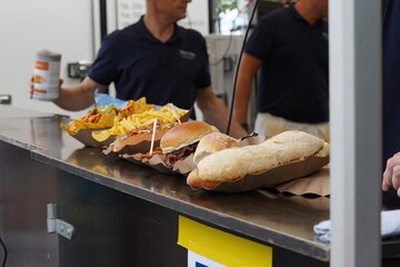Fast food such as sandwich, hamburger, hotdog, French frites, tortillas and guacamole placed respectively on paper trays and displayed on a counter of a market stall.  - obrazy, fototapety, plakaty
