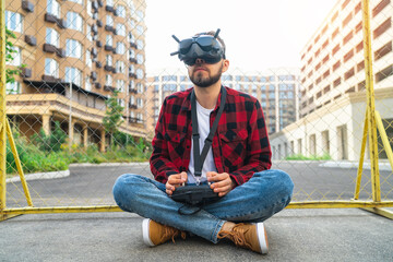 Pilot man sitting on the street road using goggles and remote controller to operate generic design fpv drone for aerial urban photography and videography - 644174379