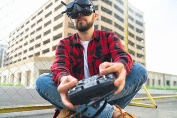 Close up portrait of casually dressed male fpv pilot operating drone using goggles nad remote...