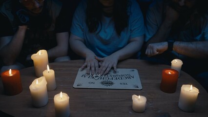 Shot capturing a group of people, friends having an ouija board session, seance, surrounded by...