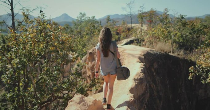 Woman tourist traveler walking Pai Canyon Kong Lan, Chiang Mai Province, Thailand. Long hair brunette with bag back view, slow motion