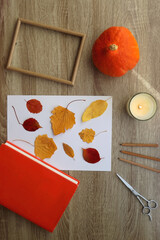 Paper with pressed colorful leaves, book, scissors, pencils, picture frame, scented candle and...