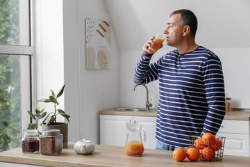 Mature man drinking orange juice in kitchen