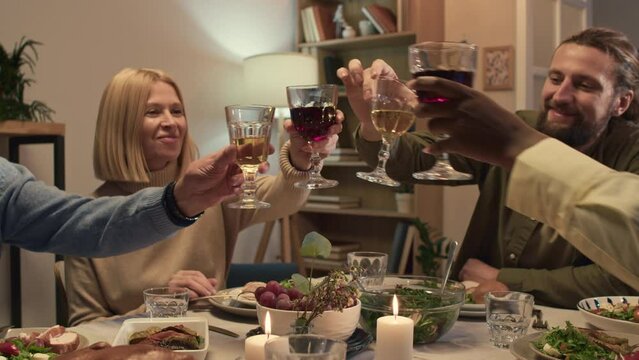 Members of family celebrating birthday and clinking glasses with wite and red wine while sitting at festive table at cozy living room