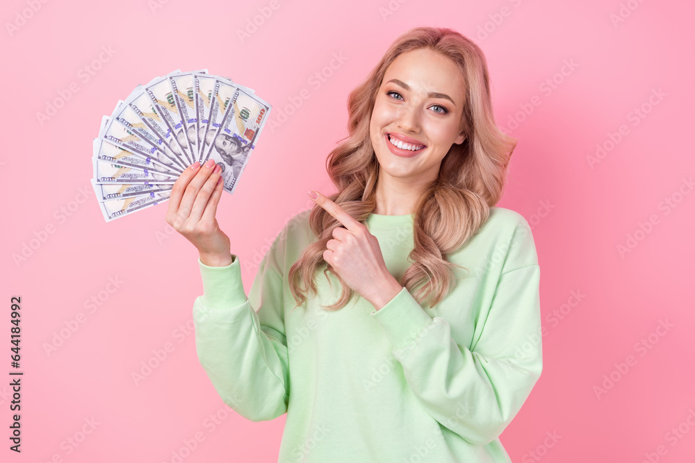 Poster Photo of gorgeous young woman wear green sweatshirt pointing finger dollars first big money lottery isolated on pink color background