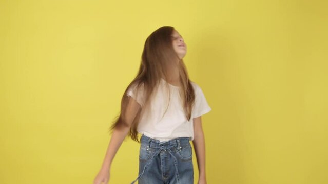 Little fun teen kid girl 7-8 years old in jeans and white t-shirt posing isolated on yellow background studio People childhood lifestyle concept. Little girl shaking her hair and smiling at camera