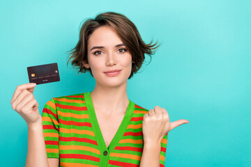 Photo of pretty shiny lady wear striped cardigan rising bank card pointing thumb empty space isolated teal color background