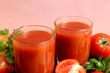 Two glasses of tomato juice stand on a wooden table.
