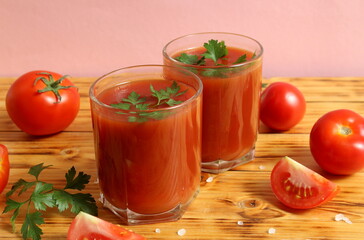 Two glasses of tomato juice stand on a wooden table.