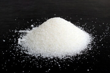 A pile of crumbly sugar in a heap lie on a black background.