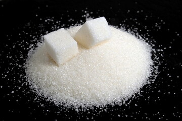 White scattered sugar with refined sugar lie on a black background.