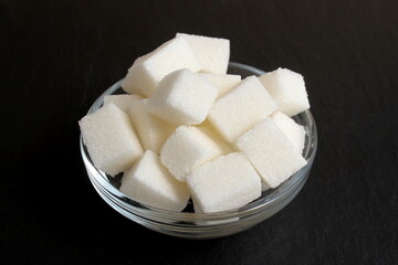 On a black background is a glass cup with refined sugar.