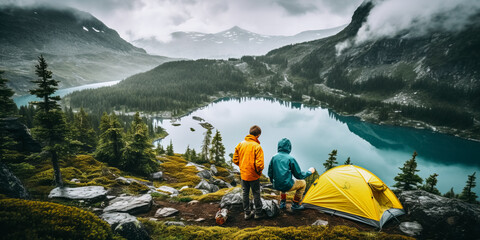 Father and son setting up tent above alpine lake during backpacking trip in rain
