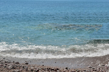 Waves on the beach. Blue water, sand and small rocks. 