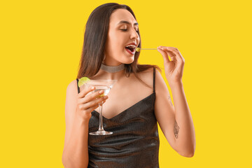 Beautiful woman with martini eating olives on yellow background