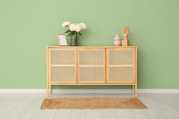 Vase of white peonies with photo frame and figurine on dresser near green wall