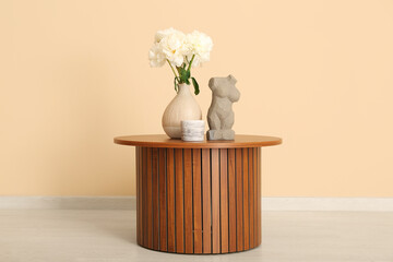 Vase of white peonies and figurine on coffee table near beige wall