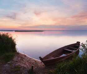 Sunset and old wooden flooding boat near the summer lake shore (Svityaz, Ukraine)
