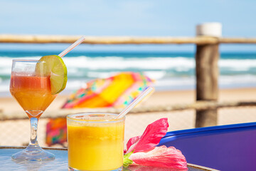 Drinks tropicais em mesa de praia no nordeste do Brasil. No fundo ondas do mar e um guarda sol...