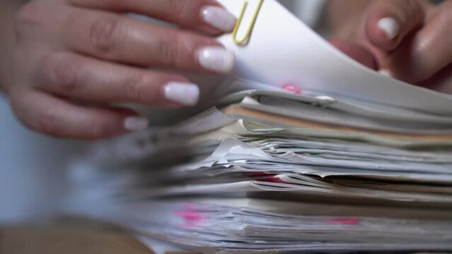 Office work with documents. Woman is looking for the right file among the papers. The manager looks through documents, contracts. Routine in the office. Close-up