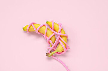 Fresh bananas in rope on pink background. Sex education concept