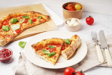 Plate with pieces of tasty pizza Margarita and basil on white table
