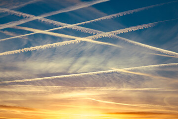 Around 10 airplane vapor trails in the sky in a diagonal pattern against a dark blue sky at sunset...