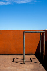 Orange wall and iron frame, with hard shadow in beautiful sunlight, with blue sky in the background. Vertical image.