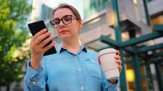 Caucasian woman in glasses stands on the street and using smartphone