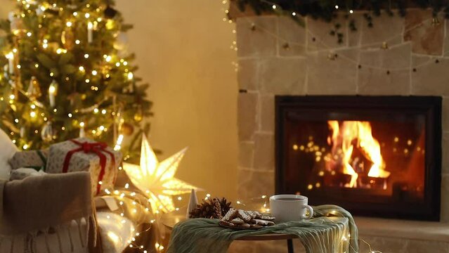 Atmospheric christmas eve footage. Stylish wrapped gifts, gingerbread cookies and tea against festive christmas tree with golden lights and cozy burning fireplace. Winter hygge