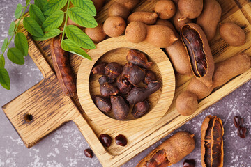 Wooden board and bowl of tasty tamarinds on grey background