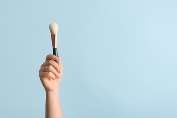 Female hand with makeup brush on blue background