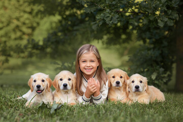 a little beautiful girl in a beige jacket and a plaid skirt with small golden retriever puppies dogs plays in the park in summer