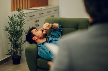 A depressed man is lying down on a sofa in a psychotherapist's office.