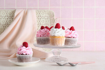 Stand and plate with tasty raspberry cupcakes on table