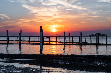 Obraz premium Sunset on the Grado Lagoon during a summer day. The sun is about to disappear over the horizon. Orange color and warm tones. A beautiful reflection on the sea. Taken near the Port.