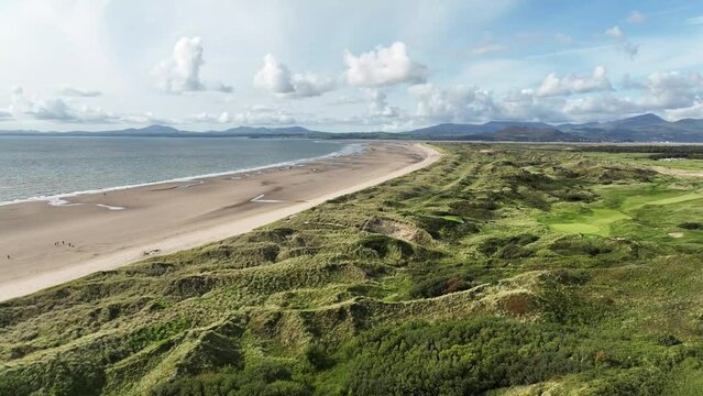 Flying over sand dune rough terrain with long grass, next to a sandy beach and blue sea and sky in Wales, UK on a hot sunny summerss day