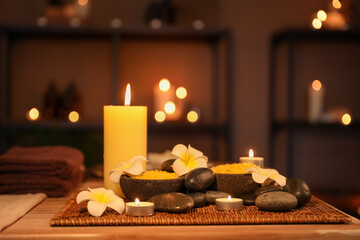 Spa composition with plumeria flowers and burning candles on table in dark salon, closeup