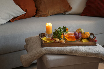 Obraz na płótnie Canvas Cup of hot tea served on a wooden tray with candle, flowers, pumpkins and biscuits on a woolen blanket at the couch, cozy autumn at home, copy space, selected focus
