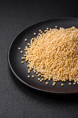 Raw ptitim pasta in a ceramic bowl on a dark concrete background