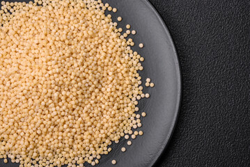 Raw ptitim pasta in a ceramic bowl on a dark concrete background
