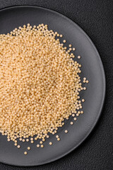 Raw ptitim pasta in a ceramic bowl on a dark concrete background
