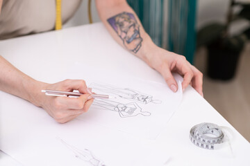 Lady designer draws clothes model on paper at table in fashion atelier tailor makes pencil sketch...